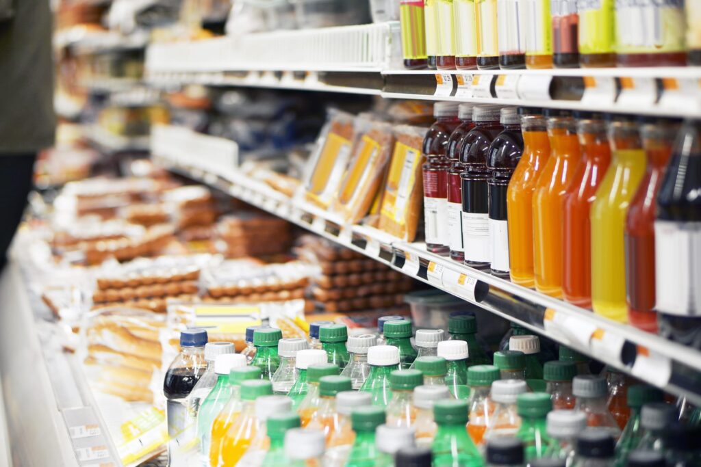 Refrigerated isle at a grocery store with products like juices, sodas, hot dogs, and others