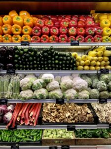 Produce isle at a grocery store, including peppers, cucumbers, and other vegetables