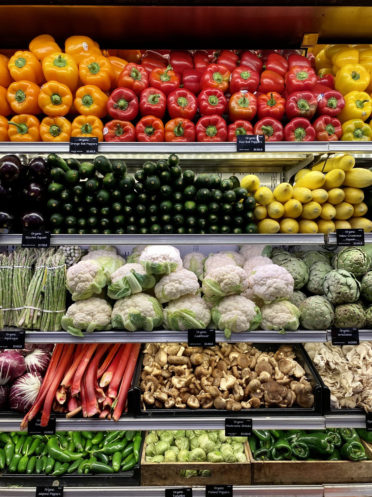 Produce isle at a grocery store, including peppers, cucumbers, and other vegetables