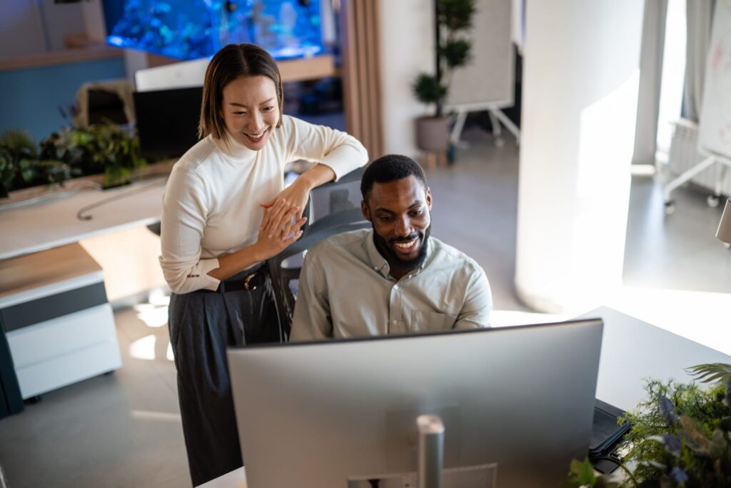 Two colleagues smiling at a computer screen together in a modern office