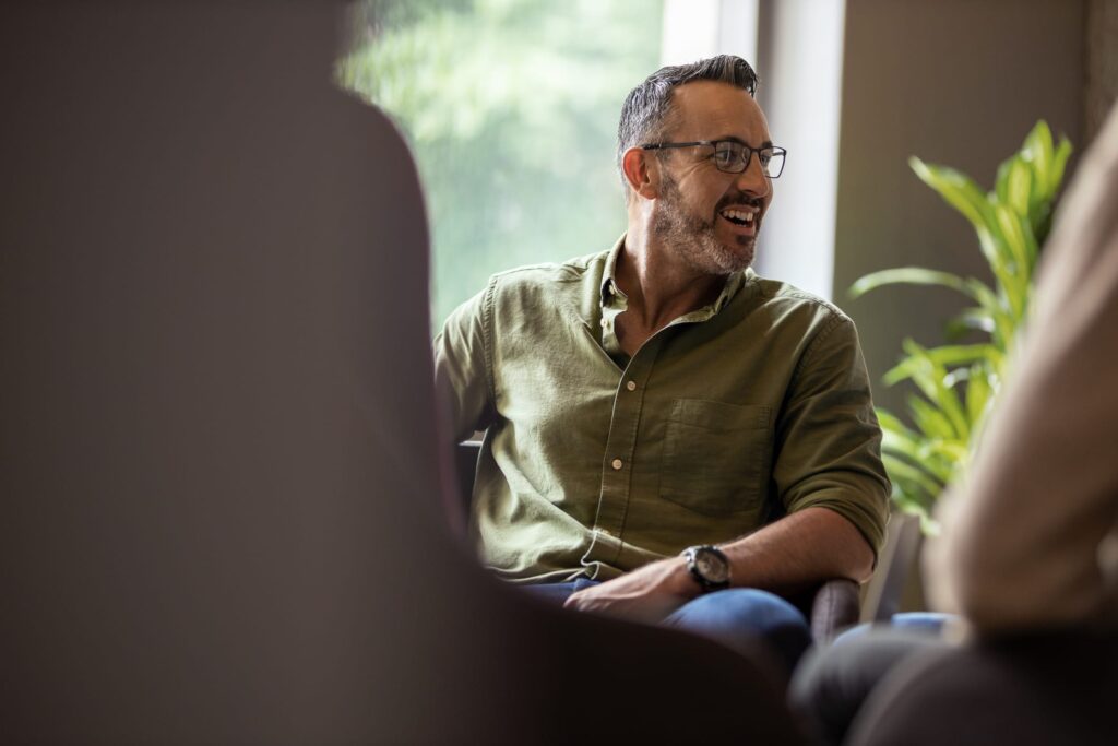 Man in a green shirt laughing during a relaxed conversation at work