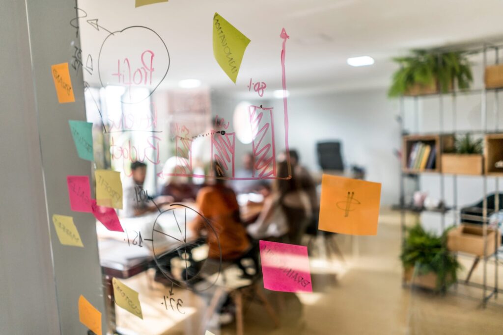 Business strategy notes and a hand-drawn growth chart on a glass wall, team meeting behind it